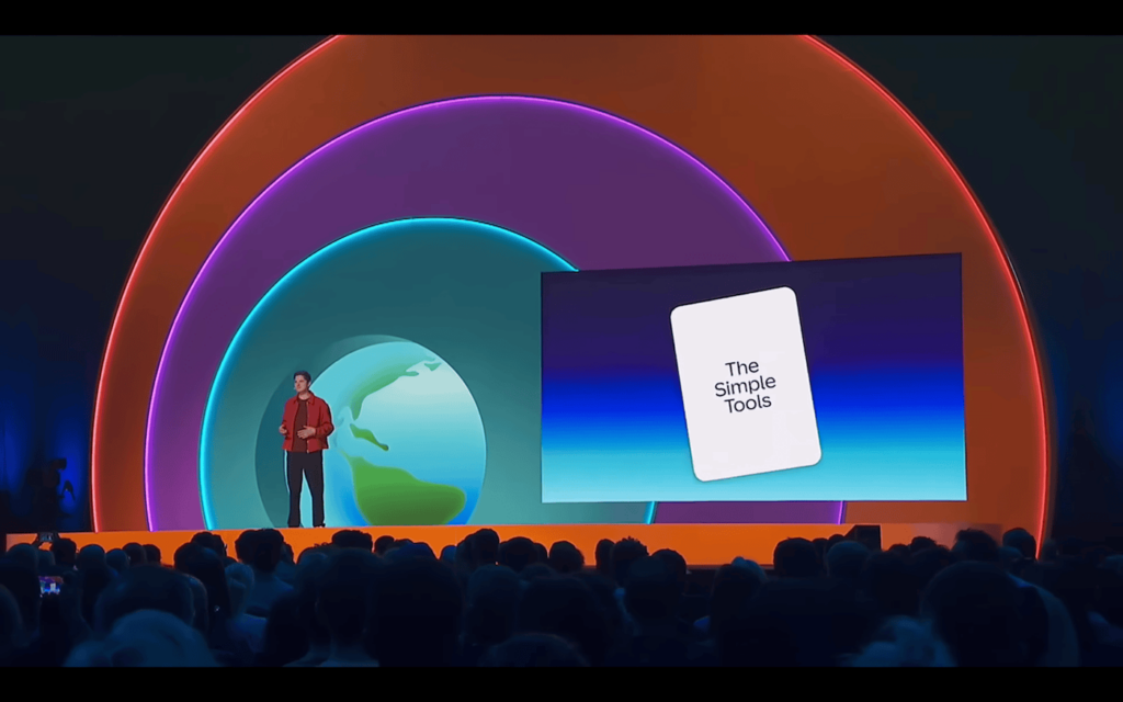 Esineja seisab suurel laval publiku ees, selja taga kujutis Maast ja erksates värvides kontsentrilised valgusringid. Paremal ekraanil on slaid tekstiga „The Simple Tools“. Tegemist on konverentsiga, mille lavadisain ja valguslahendus on visuaalselt silmapaistev.