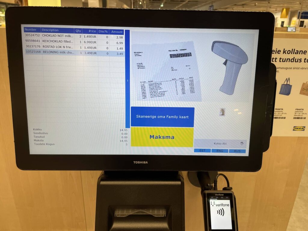 IKEA iseteeninduskassa ekraan, mis kuvab vasakul tabelina ostetud toodete nimekirja ja summade infot.  Paremal on illustratsioon kviitungist, triipkoodilugejast ja nupust tekstiga „Skaneerige oma Family kaart“ ning nupust „Maksma“. All paremas nurgas on keelevalikud: EST, ENG, RUS.