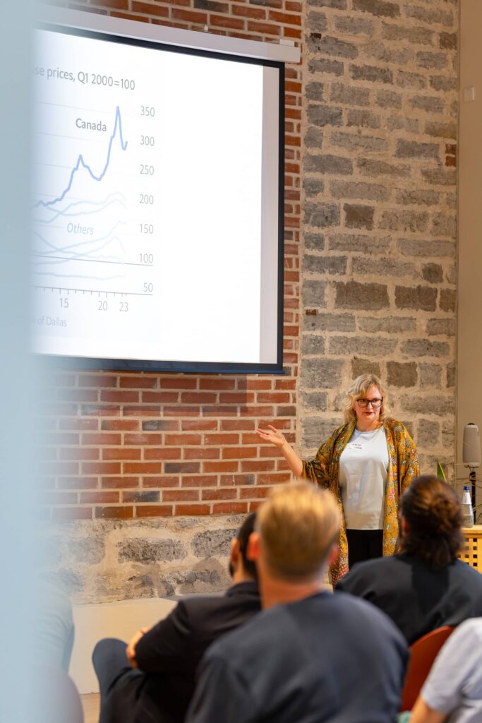 Kaisa Laur gestures towards a projected line chart of price indexes with the Canada line highlighted.