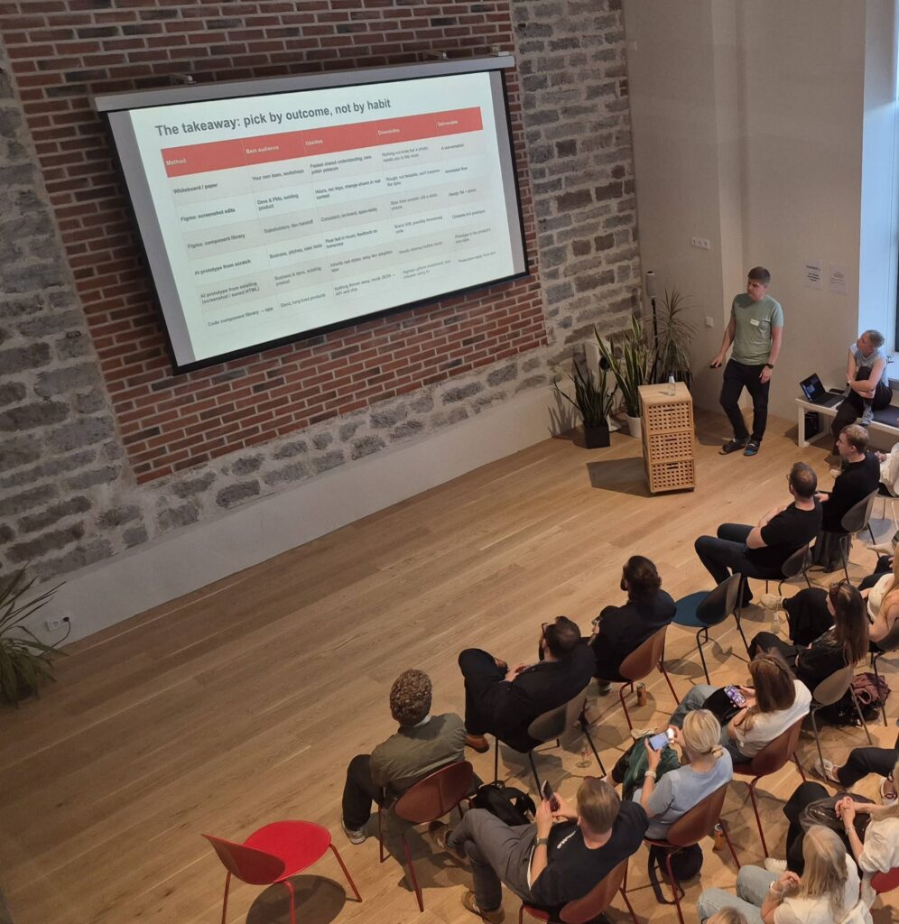 Erkki Teedla speaks beside a large projected slide headed “The takeaway: pick by outcome, not by habit”, seen from above with the audience seated in rows.